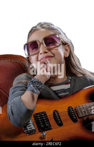 Immaginario pop-rock star, una giovane ragazza con una chitarra elettrica, occhiali da sole, appollaiati su una poltrona barocca di velluto, crogiolandosi nell'adulazione Foto Stock