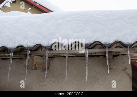 neve e ghiaccio appesi al vecchio tetto di ardesia, ghiaccio appeso dal tetto Foto Stock