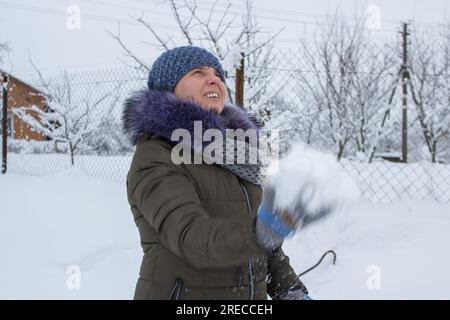 una bella donna che indossa un cappello a maglia in inverno regge una palla di neve Foto Stock