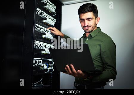 Laptop, tecnici e tecnici in una sala server per riparazioni tecniche da parte di una centralina di controllo. Tecnologia, manutenzione e maschio professionale Foto Stock