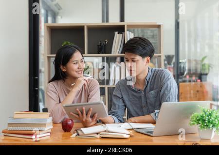 Istruzione, insegnamento, apprendimento, tecnologia e concetto di persone. Due studenti asiatici, maschi e femmine, compagni di classe con aiuta un amico a fare i compiti imparando in Foto Stock