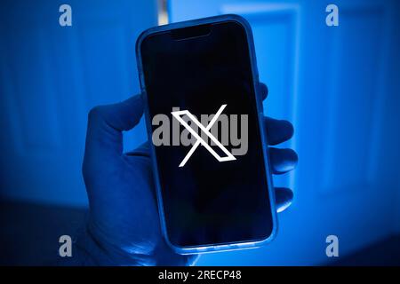 Telefono cellulare in una mano con il simbolo X, il nuovo nome della precedente app Twitter Foto Stock