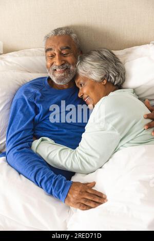 Felice coppia birazziale anziana sdraiata a letto e abbracciata a casa Foto Stock