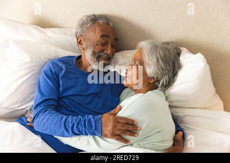 Felice coppia birazziale anziana sdraiata a letto e abbracciata a casa Foto Stock