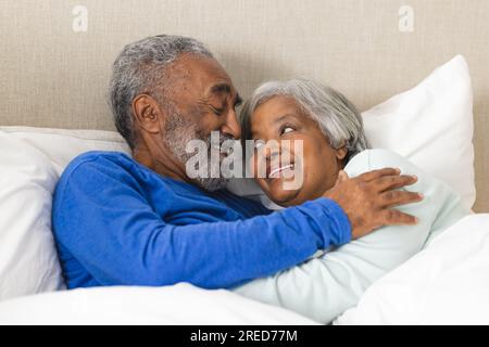 Felice coppia birazziale anziana sdraiata a letto e abbracciata a casa Foto Stock