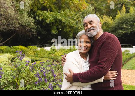 Ritratto di una felice coppia birazziale anziana che abbraccia in giardino a casa, spazio fotocopie Foto Stock