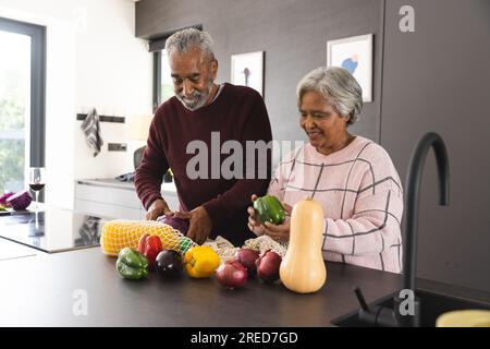 Felice coppia birazziale anziana che ha sconfezionato sacchetti di verdure in cucina a casa Foto Stock