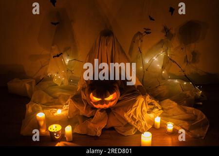 Spettrale fantasma che tiene Jack o lanterna sullo sfondo della ragnatela con pipistrelli e luci accese al buio. Decorazioni per feste di halloween dall'atmosfera spaventosa Foto Stock