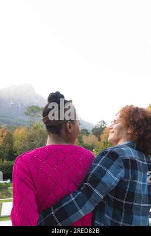 Vista posteriore di una coppia felice e variegata sul balcone che si abbracciano e sorridono a casa, spazio copia Foto Stock