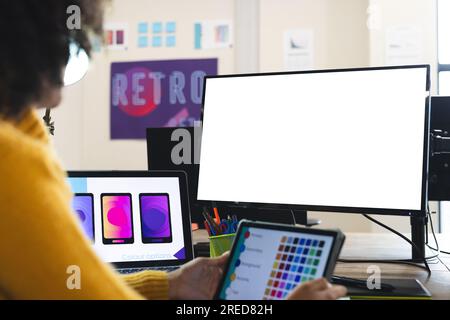 Designer afro-americana che utilizza tablet e computer con spazio per le copie alla scrivania dell'ufficio Foto Stock