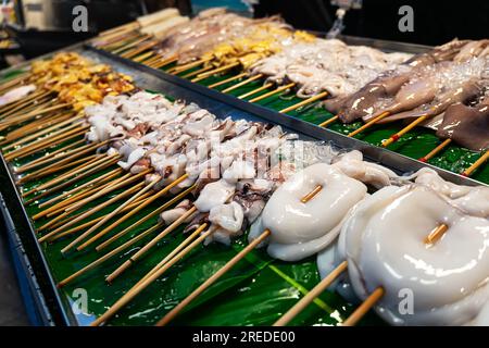 Satay di calamari crudi e una pila di cubetti di ghiaccio per mantenerlo fresco e pronto per essere grigliato nel centro del cibo di strada indonesiano Foto Stock