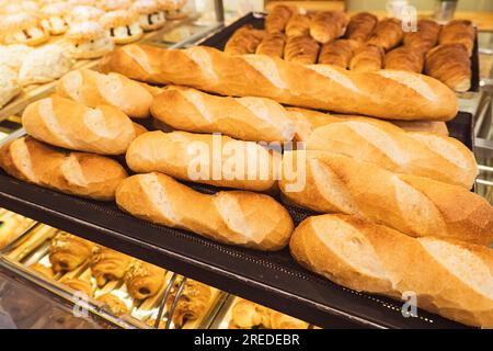 Pane appena sfornato sugli scaffali dei prodotti da forno. Varietà di pane in piena luce. Pane con crosta dorata. Panini assortiti. Foto Stock