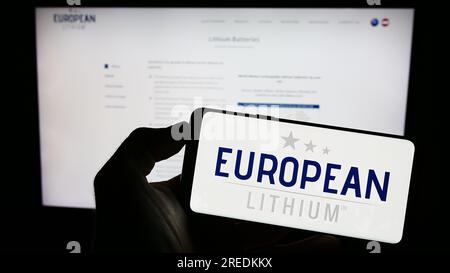 Persona che tiene il cellulare con il logo della società mineraria European Lithium Limited sullo schermo davanti alla pagina Web aziendale. Concentrarsi sul display del telefono. Foto Stock