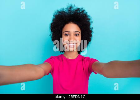 Foto di una ragazza toothy che si trasmette con afro chevelure indossa una t-shirt rosa per registrare selfie video isolati su sfondo blu Foto Stock