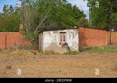 Un capannone in legno rivestito in stucco erboso erboso marrone si trova contro le pareti di cemento e gli alberi Foto Stock