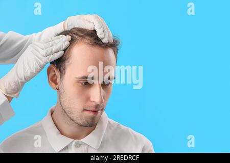 Medico che esamina i capelli del giovane su sfondo blu, primo piano Foto Stock