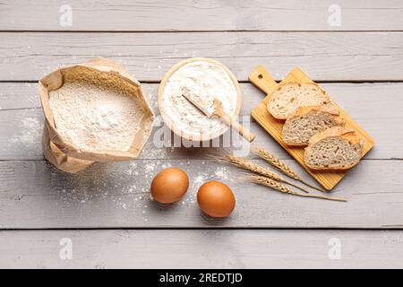 Asse di legno con fette di pane, uova e farina di grano su fondo di legno grigio Foto Stock