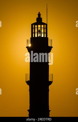 Silhouette di un faro durante un bellissimo tramonto arancione Foto Stock