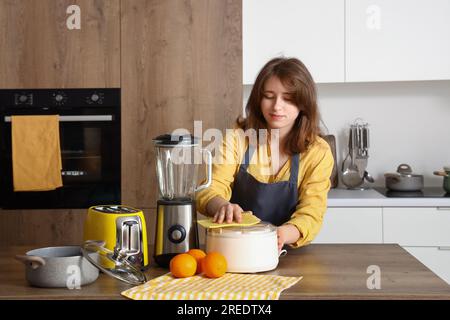 Giovane donna in cucina che pulisce la centrifuga su un tavolo di legno Foto Stock