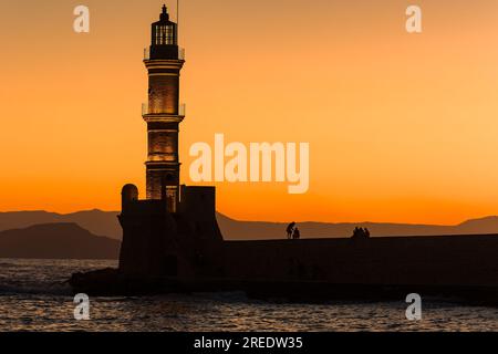 Sagoma di un antico faro di epoca veneziana e delle mura di mare durante un bellissimo tramonto arancione (la Canea, Creta) Foto Stock