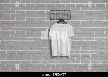 Elegante t-shirt bianca appesa a una parete di mattoni grigi Foto Stock