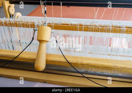 Primo piano di un telaio a pavimento che fa volare la navetta tira e deforma i fili e i cimeli per la tessitura dei tessuti Foto Stock