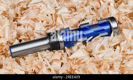 Punta fresa per rifilatura a spirale in carburo con cuscinetto in trucioli arricciati in legno heap. Primo piano dell'utensile da taglio per copia blu con lame affilate. Fresa a candela. Foto Stock