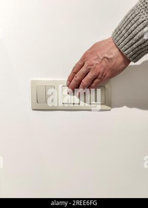 L'uomo accende la luce. La mano dell'uomo in maglione grigio preme l'interruttore della luce. Primo piano. messa a fuoco selettiva. Foto Stock