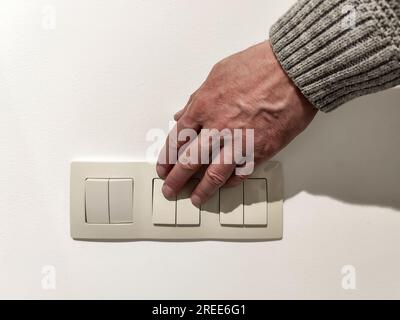 L'uomo accende la luce. La mano dell'uomo in maglione grigio preme l'interruttore della luce. Primo piano. messa a fuoco selettiva. Foto Stock