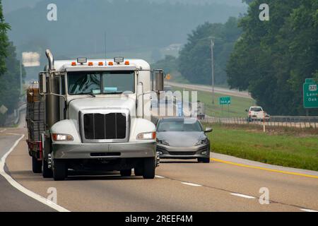 Immagine orizzontale di un pianale carico a diciotto ruote che precede il traffico in una giornata nebbiosa. Foto Stock