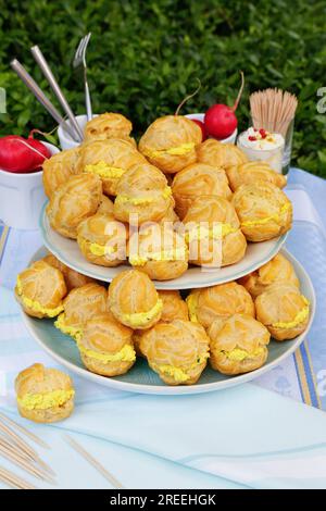 Cucina sveva, mini bocconcini di crema ripieni di formaggio cremoso di capra, eclairs di formaggio cremoso, profiterole su piatto, frollino, torte da forno Foto Stock