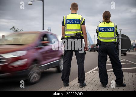 PRODUZIONE - 27 luglio 2023, Brandeburgo, Francoforte (Oder): Un'auto passa due agenti di polizia al confine tedesco-polacco. Nella prima metà del 2023 la polizia federale ha registrato più entrate non autorizzate ai confini tedeschi rispetto all'anno precedente. Foto: Hannes P. Albert/dpa Foto Stock