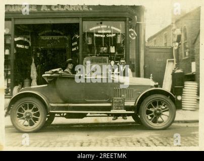 Piccola cartolina originale degli anni '1920 Maurice A. Clarke Ironmongers / ferramenta - piccola azienda a conduzione familiare - la moglie del proprietario siede in macchina, Morris Cowley 'Bullnose' apre 2 posti - possibilmente mostrando la nuova auto di famiglia. Londra Regno Unito Circa 1925. Foto Stock