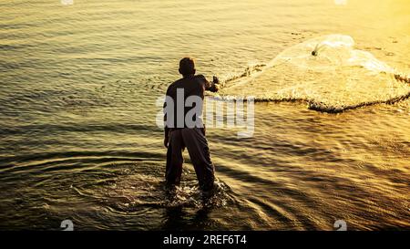 Un pescatore che getta reti da pesca all'alba sul mare di al Khobar in Arabia Saudita. Foto Stock