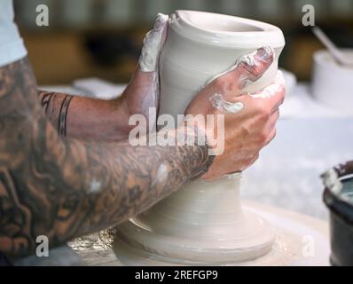 25 luglio 2023, Berlino: Il produttore Timm Langhoff usa le mani per trasformare la massa di porcellana che si sta formando in un vaso al Königliche Porzellan-Manufaktur di Berlino. La porcellana è stata fatta a mano al KPM Berlin per 260 anni. Più di 200 dipendenti lavorano attualmente al progetto "Handmade in Berlin" presso la manifattura fondata da Federico il grande. Occorrono 29 fasi di lavoro, eseguite in 14 giorni lavorativi da 25 operai della manifattura, per produrre una tazza di porcellana bianca con il reclamo KPM Berlin. Con 10 controlli di qualità, ogni oggetto viene ordinato a mano. Foto: Jens Kalaene/dpa Foto Stock