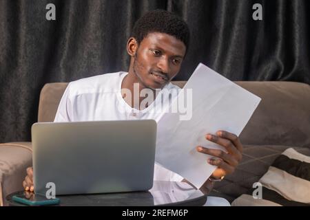 Lavorare con i documenti. Un serio imprenditore africano maschio lavora da solo in ufficio a casa tenere letto la copia cartacea del documento pensa a condizioni. Giovane concentrato Foto Stock