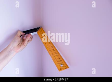 Il lavoratore tiene un angolo metallico di misurazione e misura l'angolo della parete. Finire il lavoro. Riparazione nell'appartamento, ufficio. Foto Stock