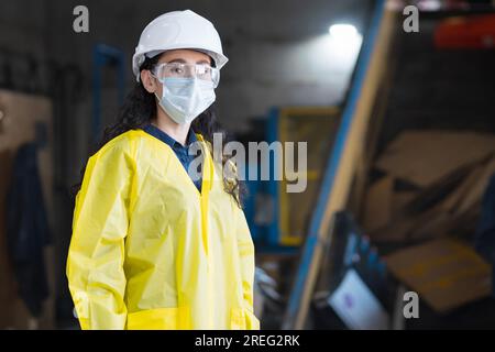 La donna in casco guarda i lavoratori che smistano i rifiuti all'impianto Foto Stock