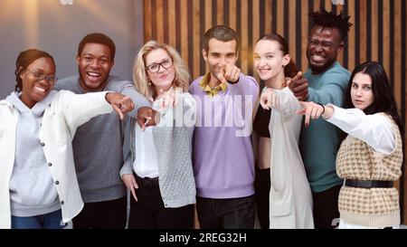 Gruppo di giovani allegri che si trovano vicini l'uno all'altro e vi indicano Foto Stock