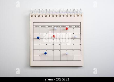 Concetto di pianificazione e pianificazione, calendario con spilla colorata su tavolo bianco. Spille ricamate sull'evento del calendario. Calendario Planner, orologio per impostare l'orario Foto Stock