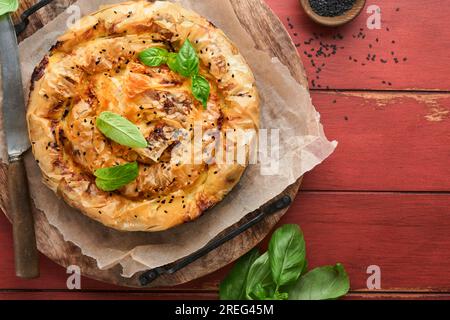 Deliziosa torta spanakopita con formaggio feta morbido e spinaci su vecchi sfondi di legno rosso. Tradizionale torta greca a spirale di pasta sfoglia spanakopita Foto Stock