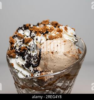 Biscotti Crunch gelato sundae serviti in un alto bicchiere di sundae con 3 cucchiai di gelato e una varietà di condimenti. Foto Stock