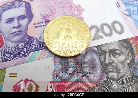 Primo piano su una moneta Bitcoin d'oro sopra una pila di banconote ucraine Hryvnia. Foto Stock