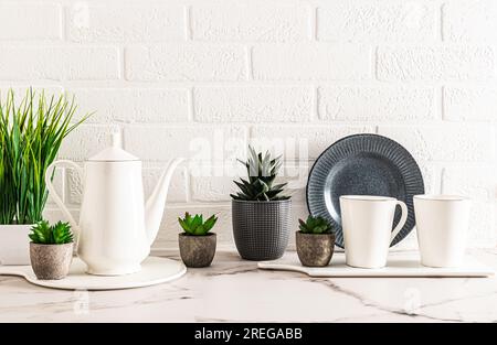 Splendido sfondo della cucina dai colori chiari con caffettiera bianca e due tazze su un ripiano in marmo con fiori al coperto in vaso. Cucina accogliente Foto Stock