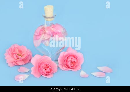 Acqua di rosa per la cura della pelle naturale in bottiglia a forma di cuore con fiori di rosa e petali su blu. Può bilanciare il ph degli oli cutanei. Foto Stock