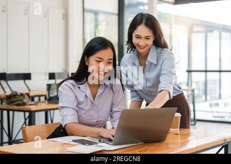 Due giovani donne d'affari asiatiche discutono di progetti di investimento e di strategia di pianificazione. Persone d'affari che parlano insieme con un computer portatile all'indirizzo Foto Stock