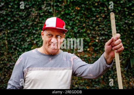 Un uomo anziano premuroso si prende un momento dal lavoro di bordo mentre tiene il rastrello Foto Stock