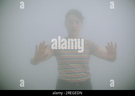 Giovane donna che cammina attraverso la nebbia in un parco Foto Stock