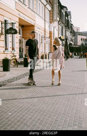 L'uomo su uno skateboard incontra una donna per strada. Coppia innamorata. Foto Stock