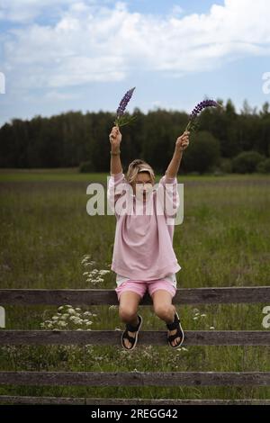 La donna in campagna siede su una recinzione e guarda il tramonto. Foto Stock